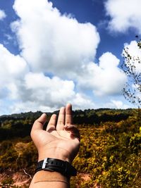 Midsection of person hand on field against sky