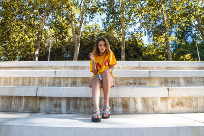 Full length of young woman sitting on steps against trees