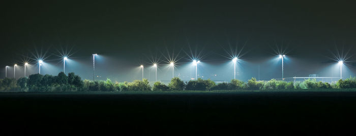 Illuminated street lights on field against sky at night