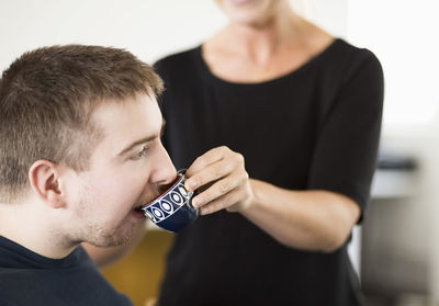 Midsection of female caretaker feeding coffee to disabled man at home