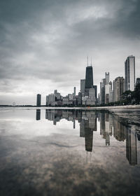 Reflection of modern buildings in river against cloudy sky