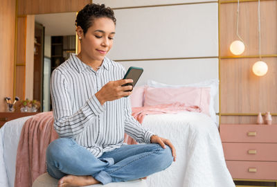 Young woman using mobile phone while sitting on bed