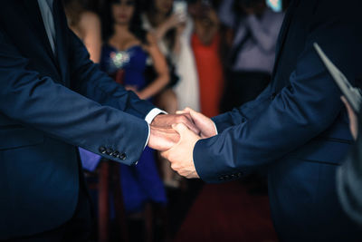 Midsection of gay couple holding hands during wedding ceremony