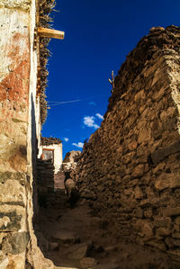 Goat walking on alley amidst stone wall against sky