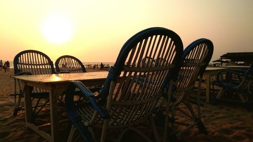 Empty chairs and table at beach against clear sky