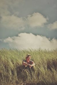 Man sitting on grassy field against sky