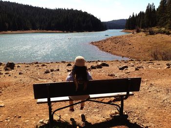 Rear view of woman sitting on bench against lake