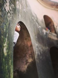 Low angle view of boy peeping from arch window on building wall