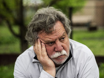 Close-up of sad senior man with hand on chin sitting in park