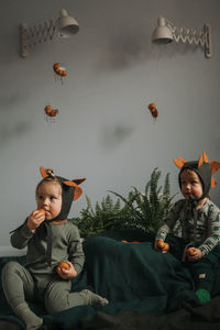 Toddler twins in funny dino costumes sitting with eggs in hands