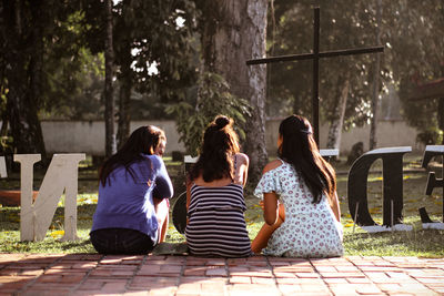 Rear view of people sitting on floor against trees