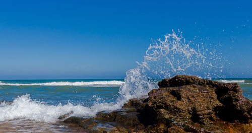 Sea waves splashing on rocks against blue sky