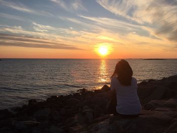 Rear view of woman looking at sea against sunset sky