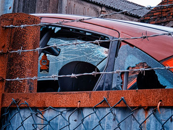 Damaged car seen through barbed wire fence