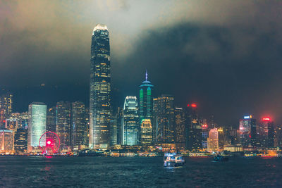 Illuminated buildings by river against sky in city