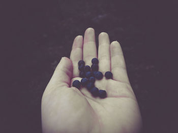 Close-up of human hand with blueberries against black background