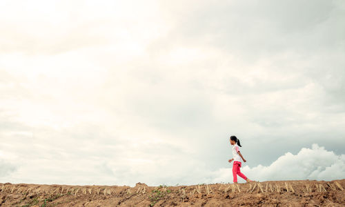 Side view of girl walking on land against sky