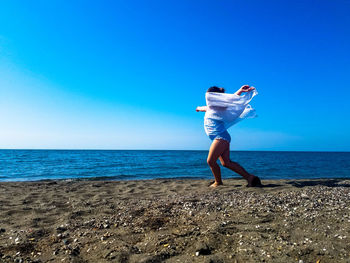 Girl standing on shore at beach against clear blue sky during sunny day