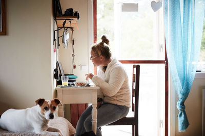 Disabled young woman using laptop at desk with dog in foreground at home