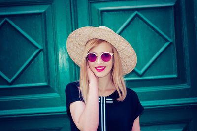 Portrait of woman in sunglasses and hat standing against door