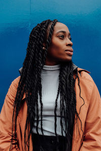 Young woman looking away while standing against blue wall