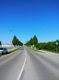 Empty road along trees and against blue sky