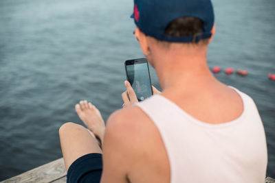 Rear view of man using mobile phone by sea