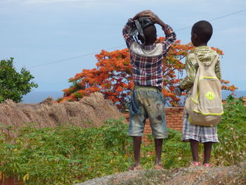 Rear view of friends standing on field against sky