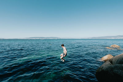 Rear view of woman swimming in sea against clear blue sky