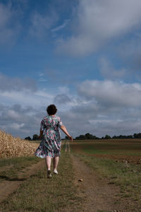 Rear view of woman standing on field against sky