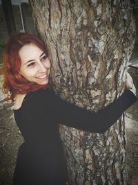 Portrait of smiling young woman standing by tree trunk