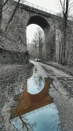 Reflection of bridge in puddle on river