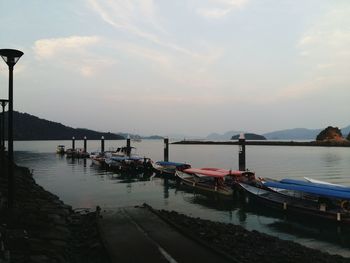 Boats moored in harbor at sunset