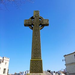 Low angle view of cross amidst buildings against clear blue sky