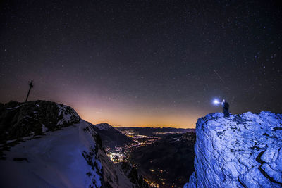 Person standing on snowcapped mountain against sky at night