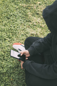 Young man sitting on the ground in the park, completely immersed in his smartphone.