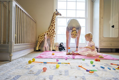 Young mother stretching while toddler daughter plays in nursery