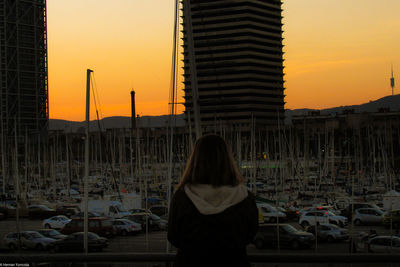 Rear view of woman standing in city against sky during sunset