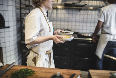 Midsection of waitress carrying food plates in kitchen at restaurant