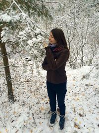 Full length of smiling woman touching tree while standing on snow covered field