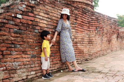 Rear view of mother and son standing against brick wall