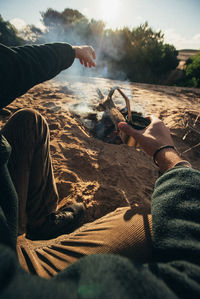 Low section of man holding smoking pipe while camping outdoors