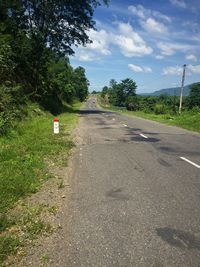 Empty road by trees against sky