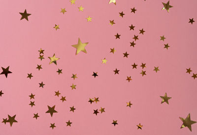 Golden stars glittering confetti on pink background. trendy festive holiday backdrop.