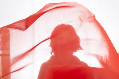 Young man with red transparent fabric in motion against white background. studio photography.