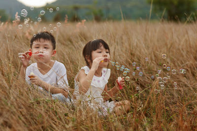 Siblings blowing bubbles on grassy field