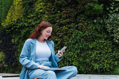 Young business woman using mobile phone while sitting outdoors