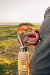 Midsection of pregnant woman holding wireless headphones and water bottle