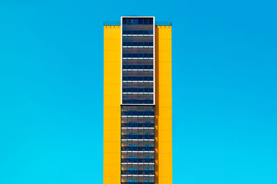 Low angle view of yellow building against clear blue sky