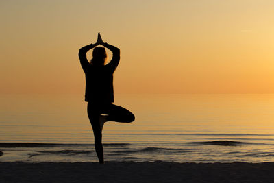 Full length of silhouette woman doing tree pose at beach against sky during sunset